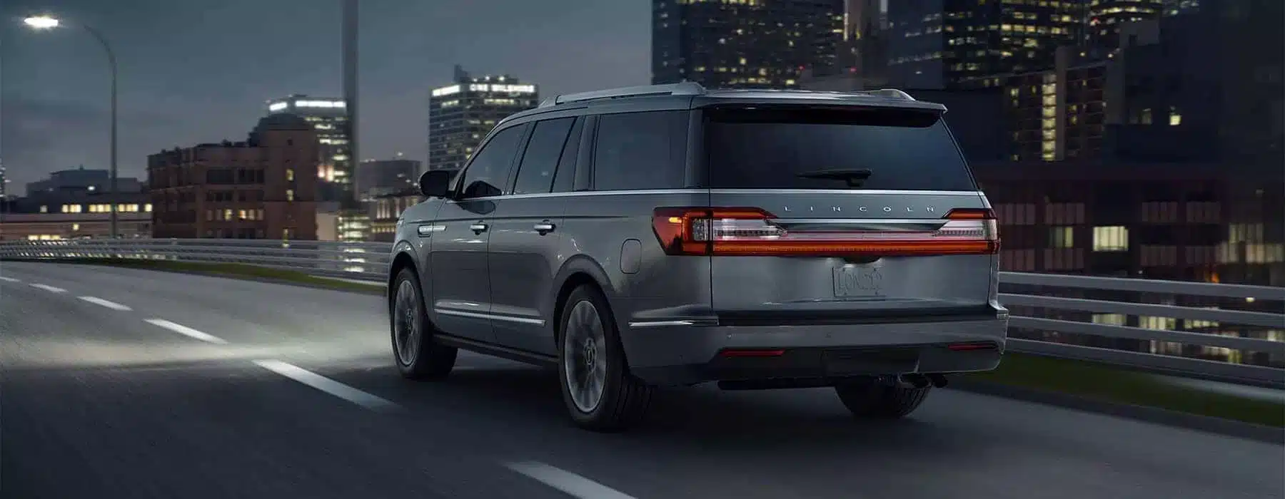 SUV driving on a city highway at night, with illuminated buildings in the background.