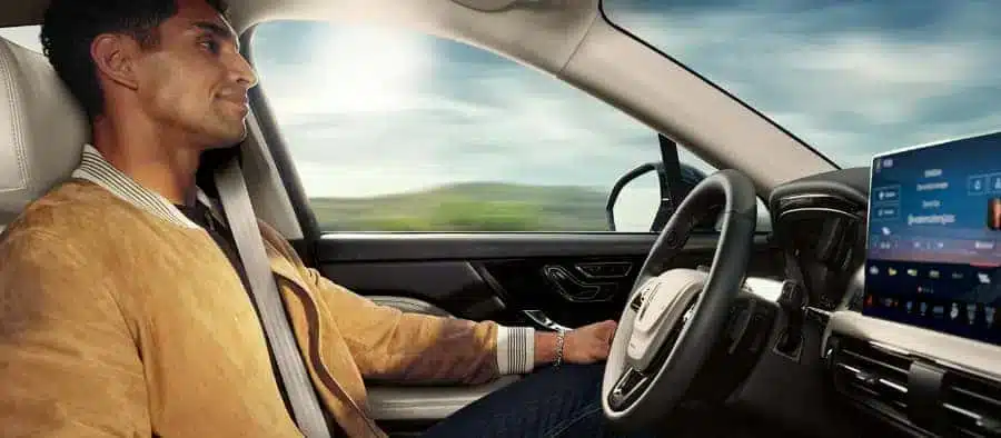 Man relaxing in a self-driving car, hands-free, with a digital dashboard displaying information.