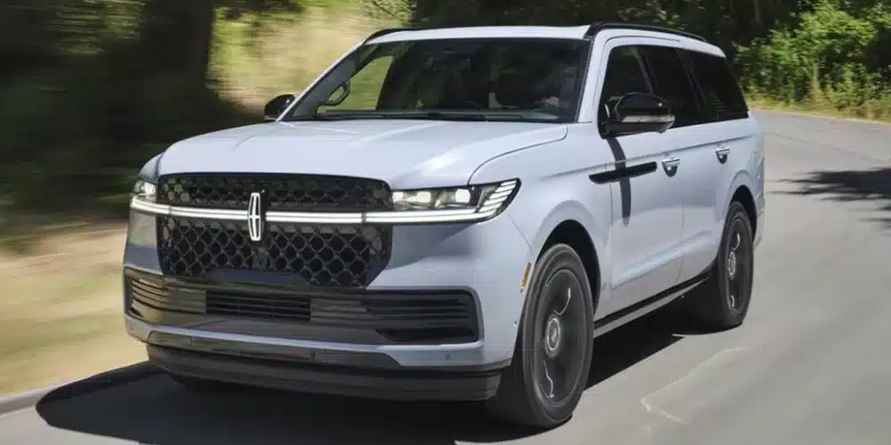 A modern SUV driving on a sunny road, surrounded by greenery, showcasing its sleek design and style.