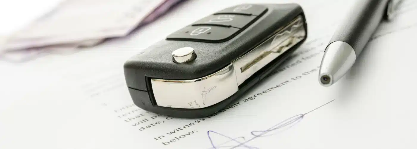 Car key and pen on signed contract, suggesting vehicle lease or purchase agreement.