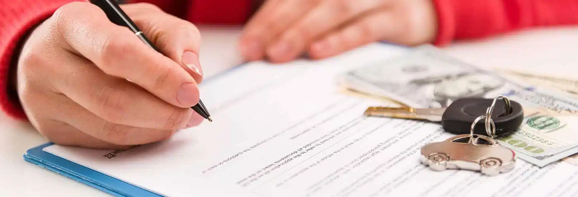 Hand signing a contract with car keys and cash nearby, symbolizing vehicle purchase or lease.