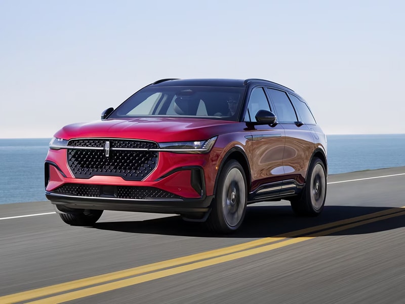 Red SUV driving on a coastal highway under a clear blue sky.