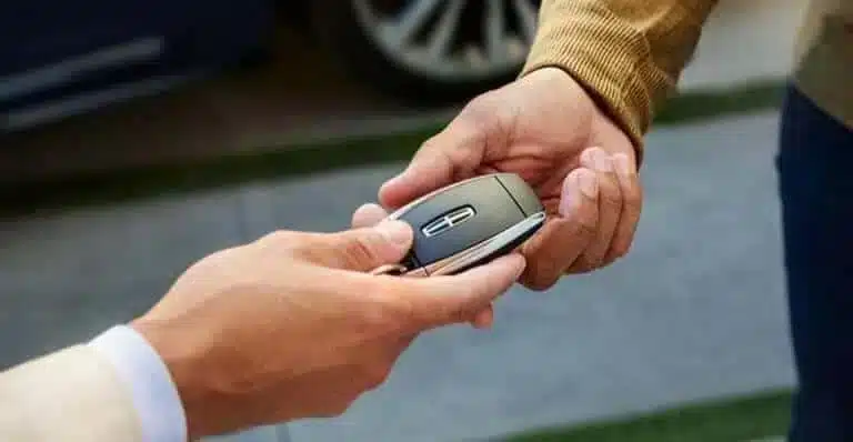 Two hands exchanging a car key fob, suggesting a vehicle transaction or rental.