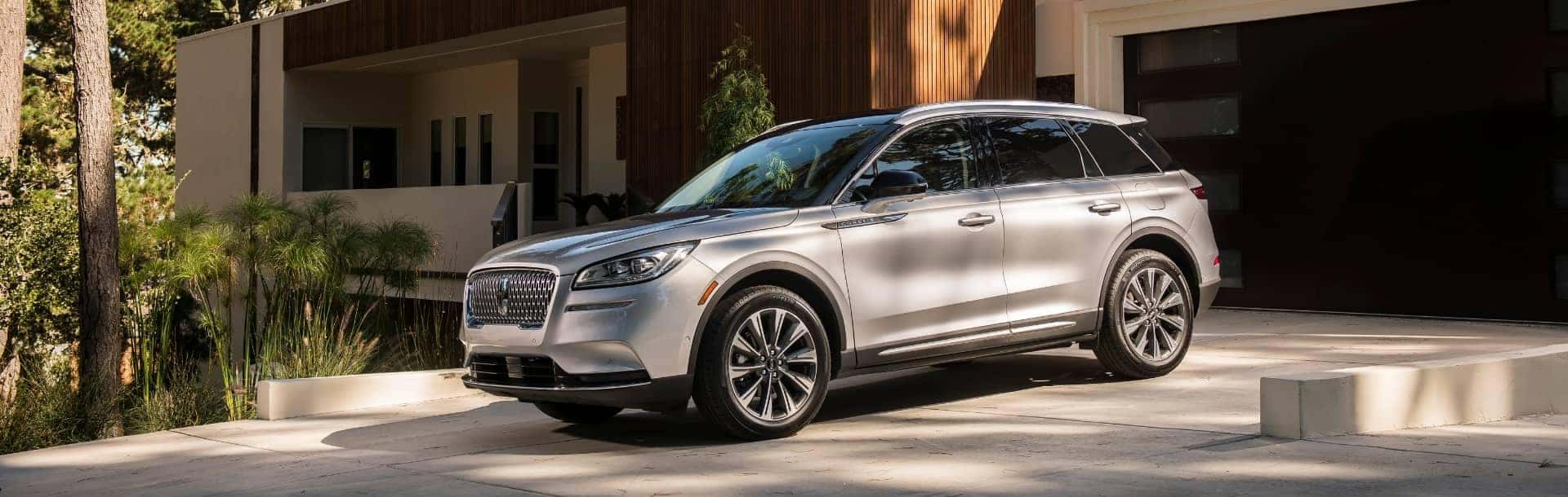 Silver SUV parked in a modern driveway surrounded by trees and contemporary architecture.