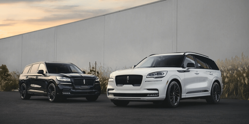 Black and white luxury SUVs parked in an industrial area at sunset.
