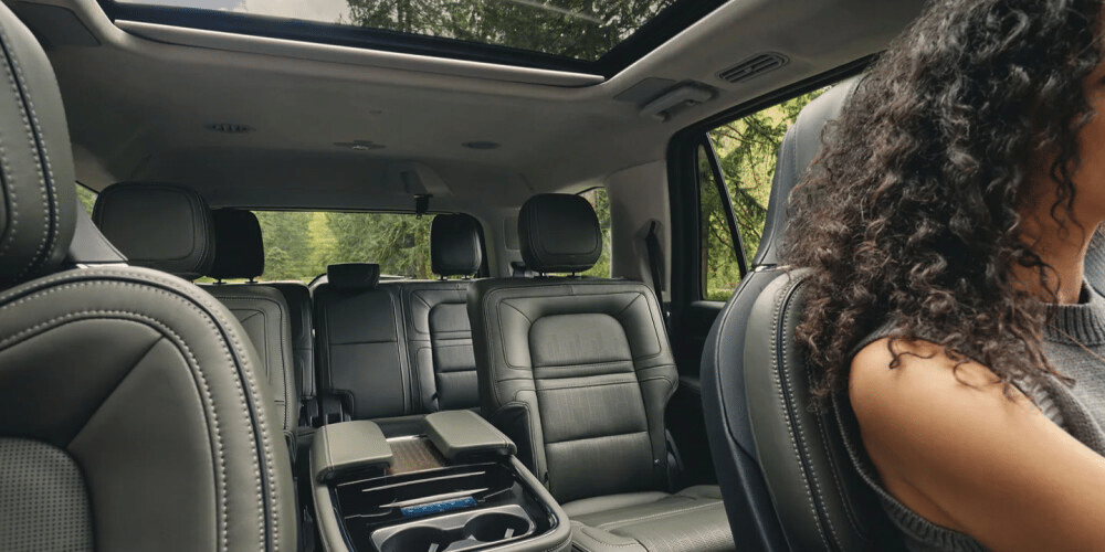 Interior of a luxury SUV with leather seats and sunroof, woman driving through a forested area.