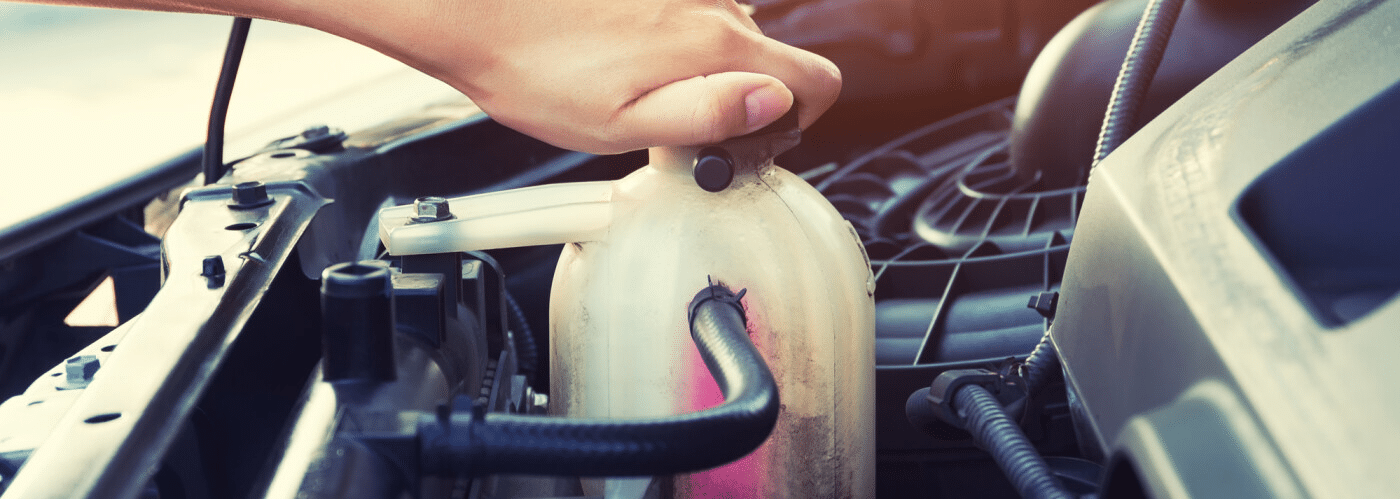 Hand checking car engine coolant reservoir under hood in sunlight.