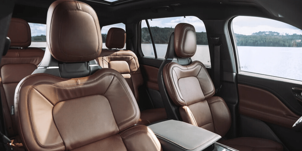 Luxurious car interior with brown leather seats and a scenic lake view outside.