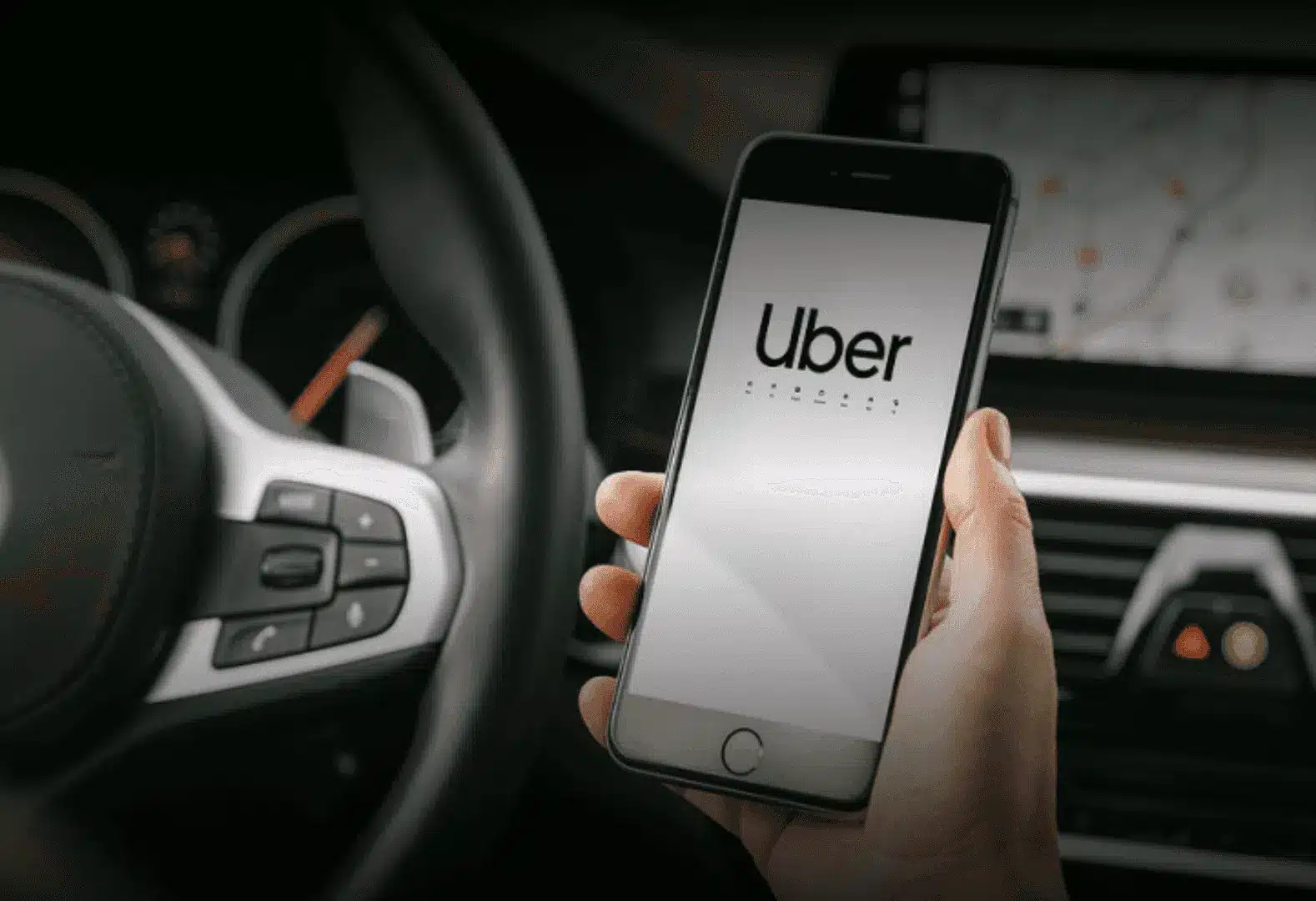 Hand holding a smartphone displaying the Uber app inside a car with visible steering wheel.