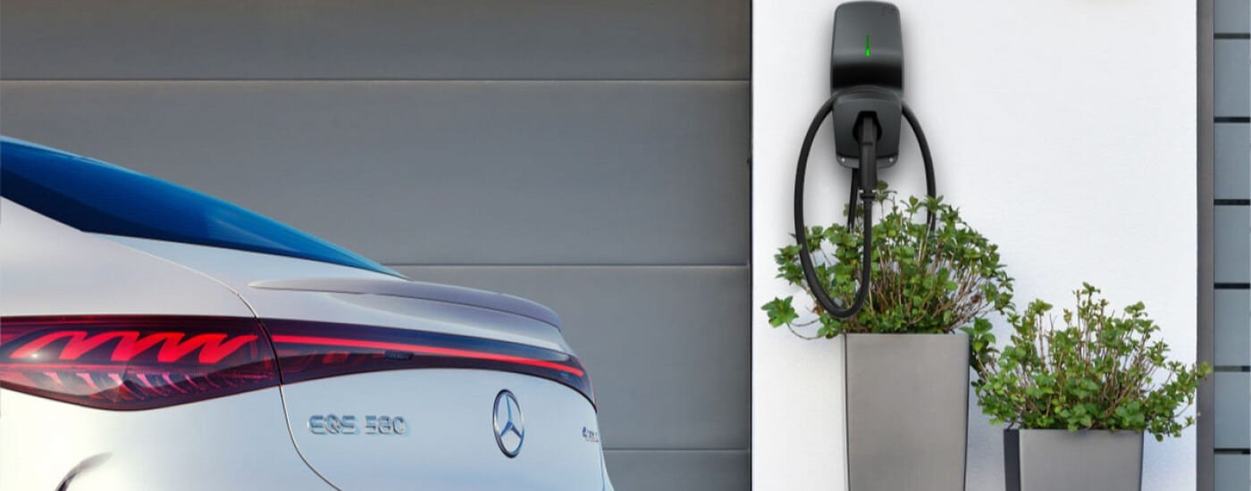 Mercedes EQS 580 rear near an EV charging station and planters against a modern garage.
