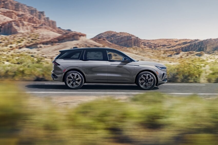 SUV driving on a highway through a desert landscape with rocky hills in the background.