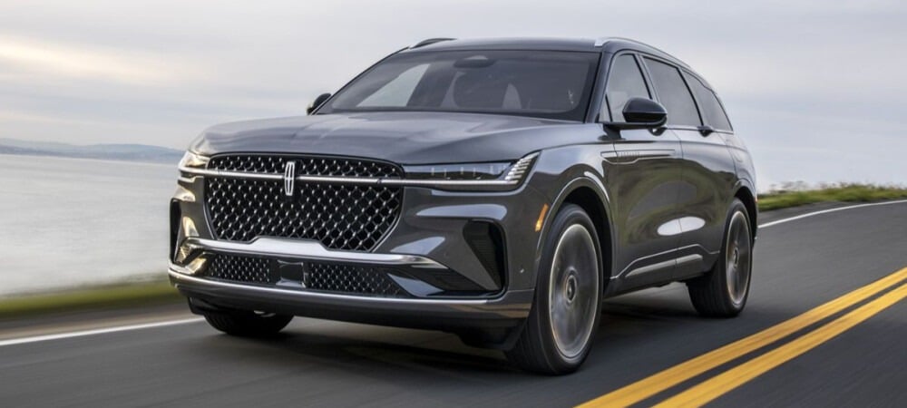 Gray Lincoln SUV driving on a coastal road, showcasing sleek modern design and luxury features.