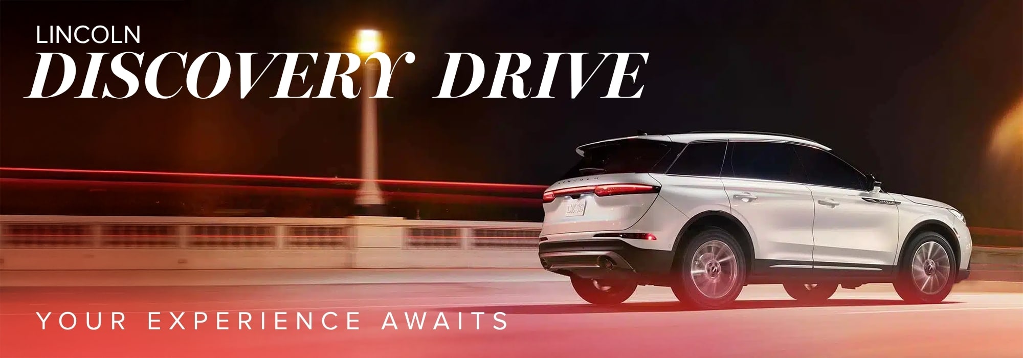 White Lincoln SUV on a lit road at night with "Lincoln Discovery Drive" and "Your Experience Awaits" text.