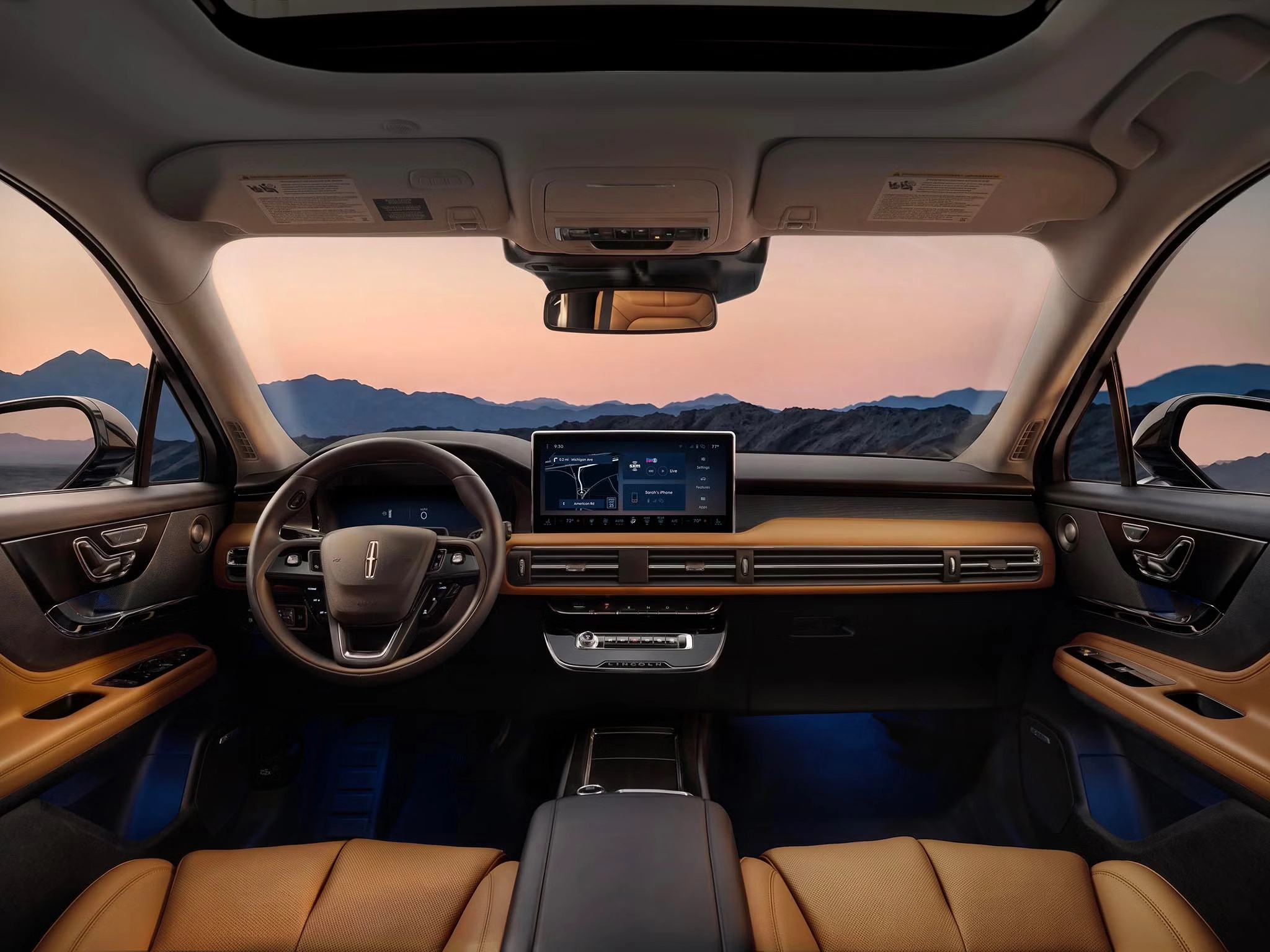 Luxury car interior with leather seats, digital dashboard, and sunset mountain view through the windshield.