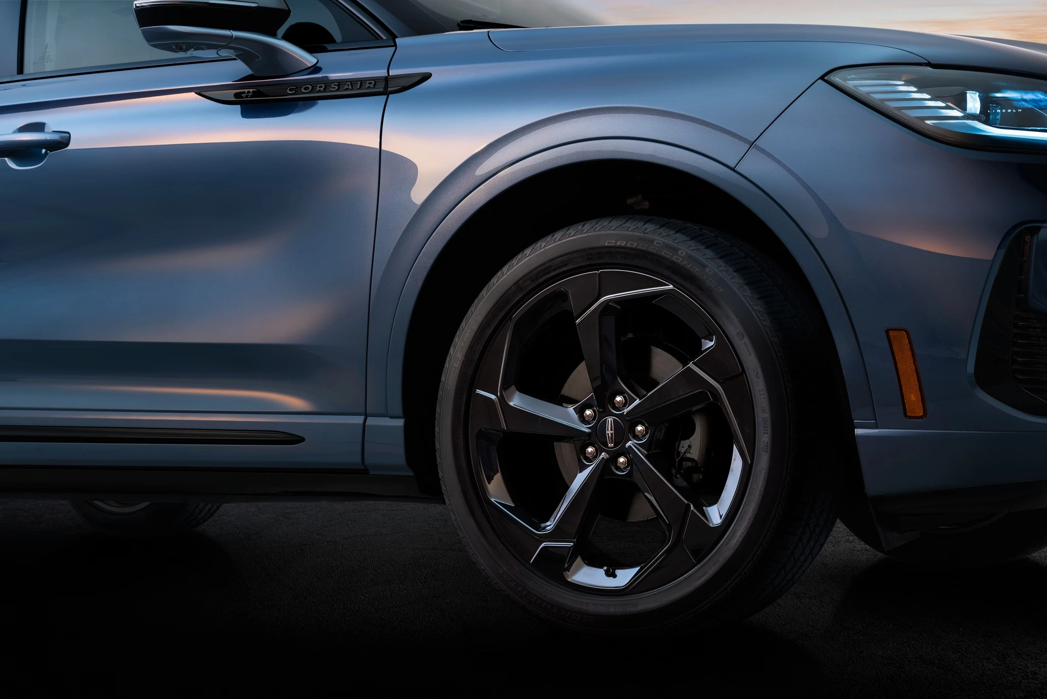 Close-up of a blue car with sleek design, highlighting the alloy wheel and side mirror.